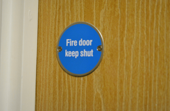 A door with a blue sign saying ‘fire door keep shut’ to show the hazards that fire stopping surveys can identify.
