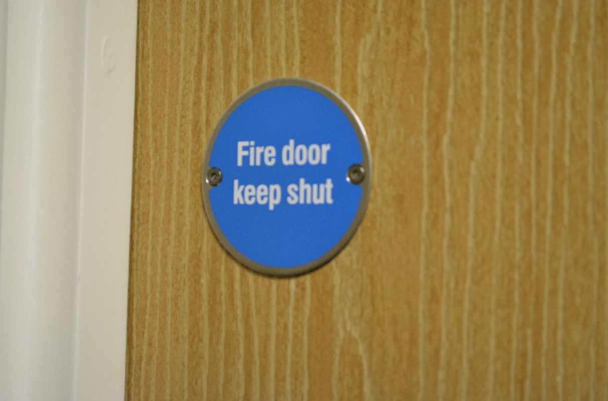 A door with a blue sign saying ‘fire door keep shut’ to show the hazards that fire stopping surveys can identify. 